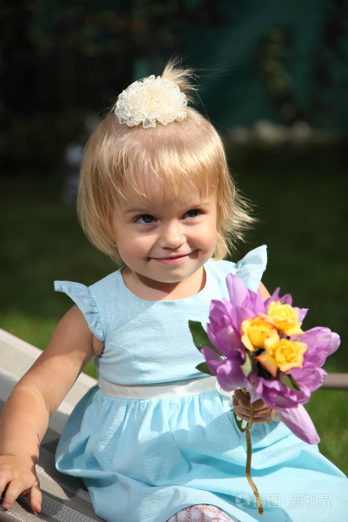 甜甜微笑的小女孩与长长的金发,坐在草地中夏公园,特写室外肖像上.