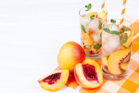 桃花与冰柠檬水和薄荷叶。自制柠檬汁的成熟油桃和白色和橙色成熟。桃花茶两杯。清爽的夏季饮料，在白色的木制背景