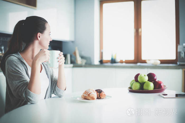 在厨房的桌子和甜牛角喝茶的女人