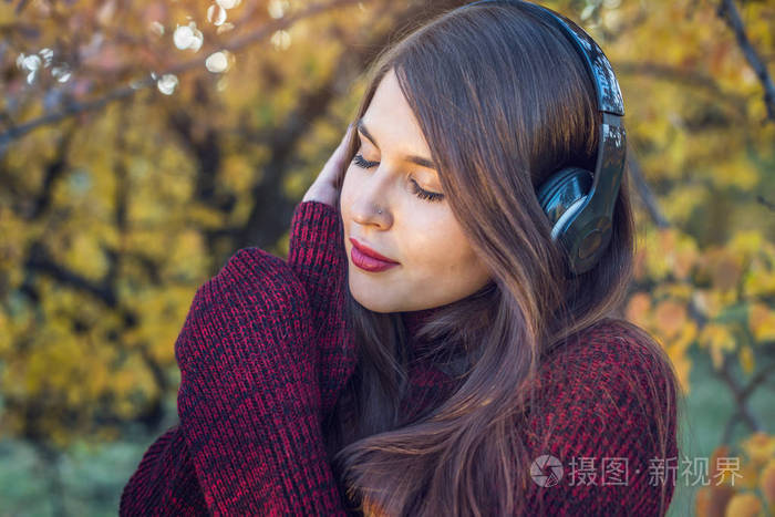 在秋季公园的妇女站在听音乐与她的耳机概念好心情喜爱音乐愉快的时间