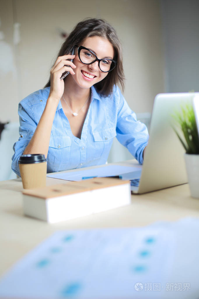 美丽的年轻业务谈的女人坐在办公室桌前在手机上女商人