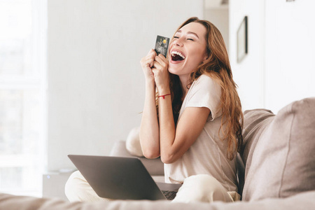幸福的女人，与信用卡和笔记本电脑坐在沙发上