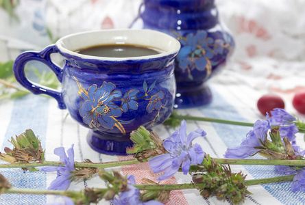 蓝杯咖啡茶饮菊苣菊苣花 绣花的布背景上的热饮料