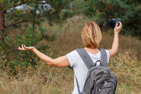 年轻的女士拿着数码相机走在森林里