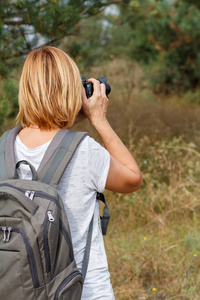 年轻的女士拿着数码相机走在森林里