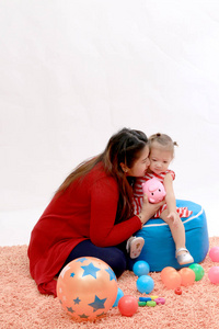 快乐的年轻孕妇，与红色针织毛衣和自己的宝贝女儿坐在橙色地毯地板用在家里的玩具玩。家庭 婴儿和新生儿的概念