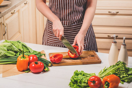 年轻的女人在家里的厨房里做饭。一个女人用一把刀切辣椒和蔬菜