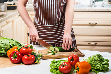 年轻的女人在家里的厨房里做饭。一个女人用小刀切黄瓜和蔬菜