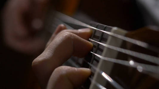 吉他手手玩吉他的特写。近摄镜头的一个人用他的手指上的吉他演奏的苦恼