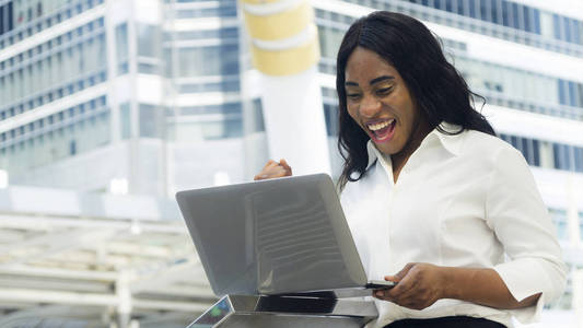 快乐和自信的业务非洲女人的画像在户外与城市空间的背景下使用电脑笔记本