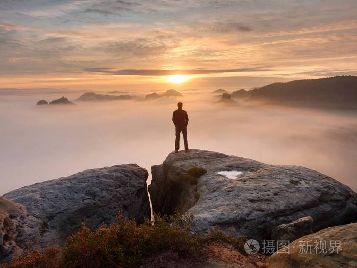 男子站独自在岩石的山峰上望着秋天太阳在地平线上的徒步旅行者美丽的