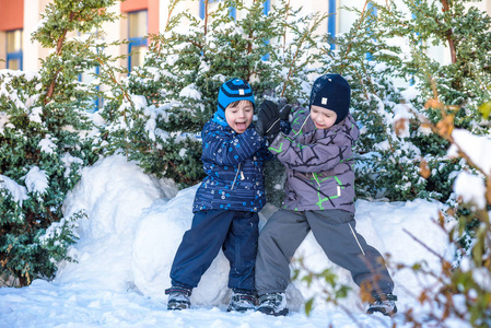 两个小家伙男孩在颜色鲜艳的衣服在降雪期间在户外玩。积极的休闲活动，与孩子在天冷的冬天。快乐的兄弟姐妹和双胞胎玩雪