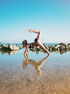 年轻的白种人女子泳装练瑜伽在海水 湖泊或河流中。美丽的倒影。复杂的体式，平衡。健身 运动 瑜伽和健康的生活方式的概念