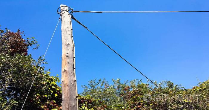 带电线的旧木杆.在有蓝天的乡村道路内的电线杆