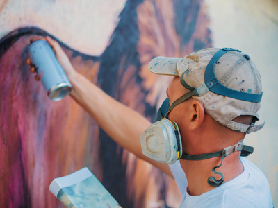 街头的墙上的涂鸦艺术家绘画。气溶胶喷雾瓶壁附近的男人。在绘制彩色狮子的防护面具的年轻才华的人