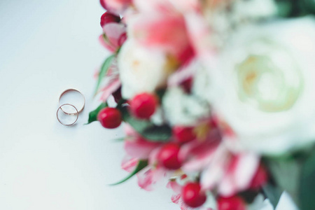着一束美丽的鲜花的新娘的白色桌子上的黄金结婚戒指。