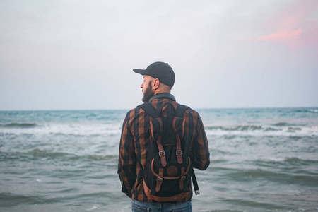 一个年轻的白人游客男子站海洋背景黎明时分。旅游和生活方式的概念