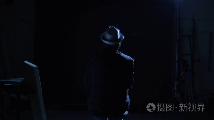戴着帽子的男人坐在椅子上,在黑暗中