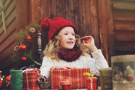 快乐的孩子女孩顶红色的帽子和围巾圣诞礼物包装在新年和圣诞节装饰的舒适的乡间别墅。与孩子们假期的筹备工作