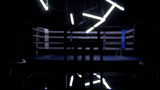 拳击和两把椅子与表暗背景。定期拳击包围蓝色绳聚光灯聚光灯下的视图。拳击台周围的灯光秀