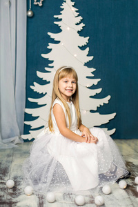 在圣诞树的背景上的白色连衣裙的女孩