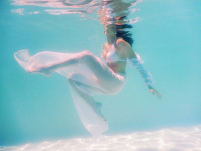 女人美丽的身体在水下游泳时穿白色礼服