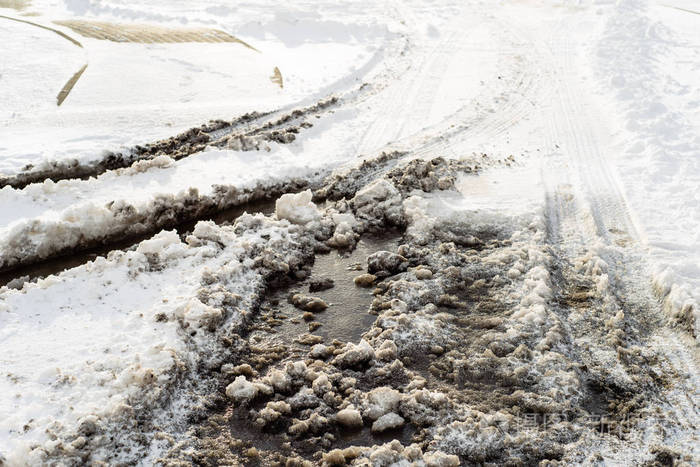 在路上,轮胎轨道与水坑泥在融化的雪纹理的冬天