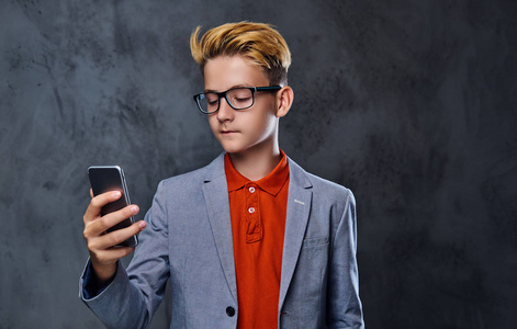 一个男孩穿一件夹克和眼镜拥有智能手机