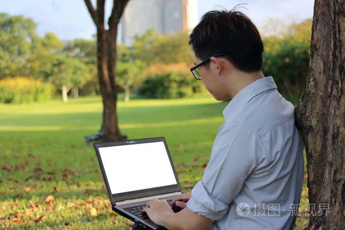 英俊的年轻男子正在用笔记本电脑为他的工作在城市公园