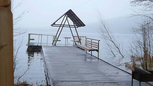 在湖，森林湖岸雨和雪的码头。湖，森林里的镜子表面覆盖着第一场雪。在水中，美丽的山景观的反射。树倒下