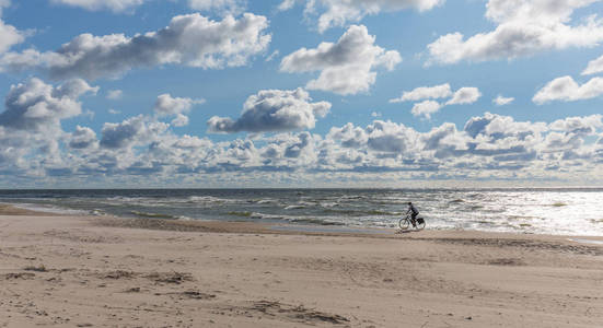 多云天空下空旷的海滩, 孤独的骑自行车者