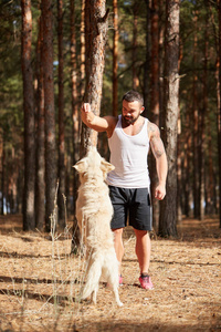 英俊的年轻男子与一只拉布拉多犬在户外在森林里