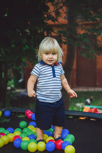 可爱的金发男孩在绿色庭院背景上玩彩色球。