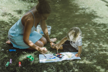 可爱的金发男孩和年轻的母亲在户外草地上画画