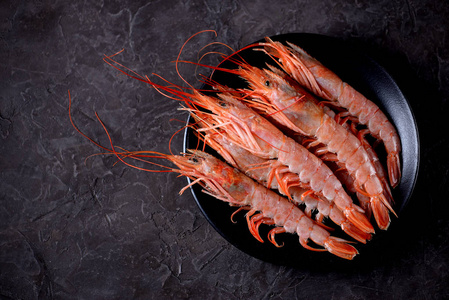 生鲜虾在烧焦的黑色背景上的黑色板上.顶视图照片