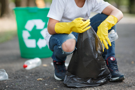 双手戴黄色手套，拿起空瓶塑料进入垃圾袋上沥青志愿者和纯度的概念。 环境保护。