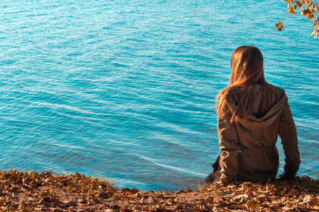 后视图的女人坐在湖边，感到孤独
