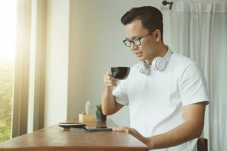 亚洲的年轻男子，喝着咖啡，在 coff 中使用数字平板电脑