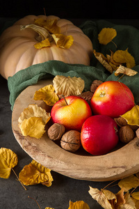 秋天的餐苹果，坚果，南瓜和黄色叶。黑暗的背景和目标