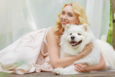 金发女孩躺在户外用一只手中的白狗