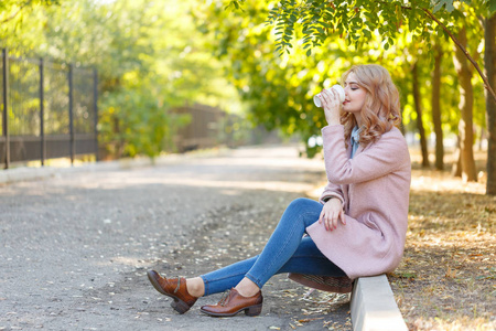 美丽的金发女郎正坐在路边和咖啡在公园