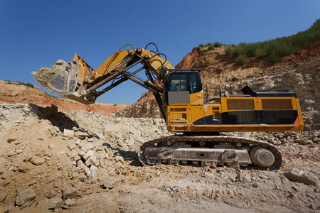 关闭巨大的挖掘机装载地面在蓝天和沙石场的背景。