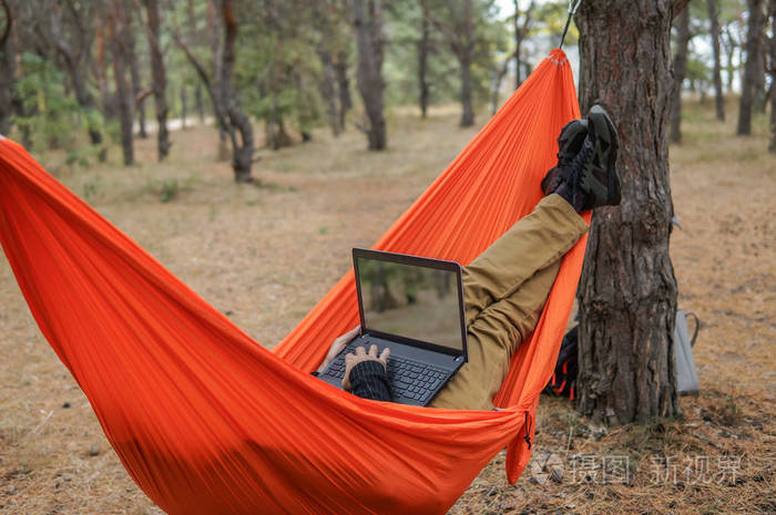 男子徒步旅行者放松和笔记本在吊床上，在国家森林公园的工作。从办公概念