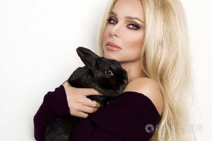性感金发碧眼的女模特站在白色背景上抱着一只兔子