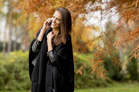 年轻的 womanusing 手机在秋天的公园