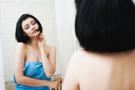女孩走出一条毛巾在浴室，在镜子里看着自己