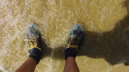 男人的腿穿着运动鞋.人站在海边沙浪湿运动鞋旅行休息照片