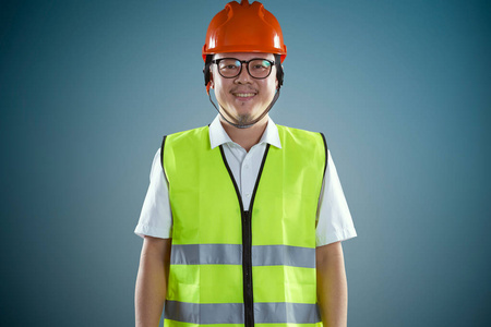 年轻的亚洲建筑工人戴着蓝色背景的安全帽。
