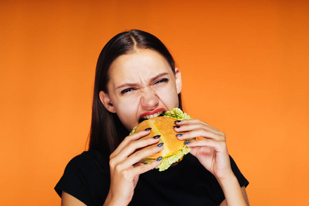 生气的女孩在她的手吃一个汉堡