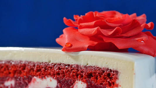 白色蛋糕巧克力饰品与红色小杏仁饼上深蓝色背景中上涨。食用红玫瑰装饰的蛋糕关闭
